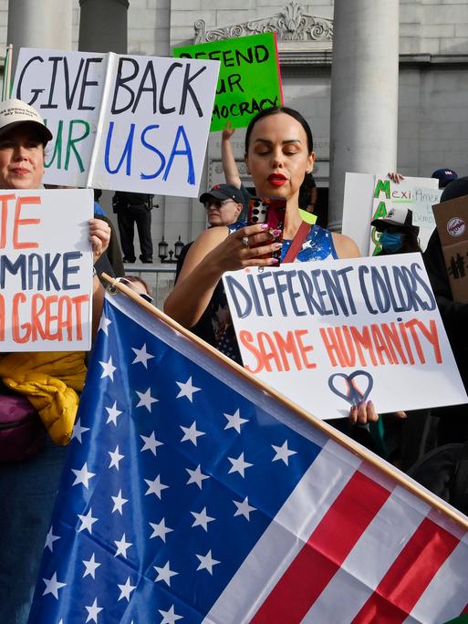 Menschen protestieren und halten Schilder. Auf einem steht "Hate won't make America great again". Die Proteste richten sich gegen die Politik Donald Trumps. Die Menschen stehen vor dem Rathaus in Los Angeles.