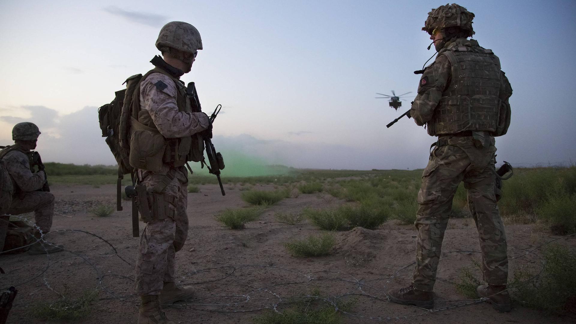 Ein Bild aus dem Jahr 2017 zeigt britische und US-amerikanische Soldaten in Afghanistan. Sie stehen bewaffnet auf einem Feld, im Hintergrund fliegt ein Helikopter. Ein Bild aus dem Jahr 2017 zeigt britische und US-amerikanische Soldaten in Afghanistan. Sie stehen bewaffnet auf einem Feld, im Hintergrund fliegt ein Helikopter.