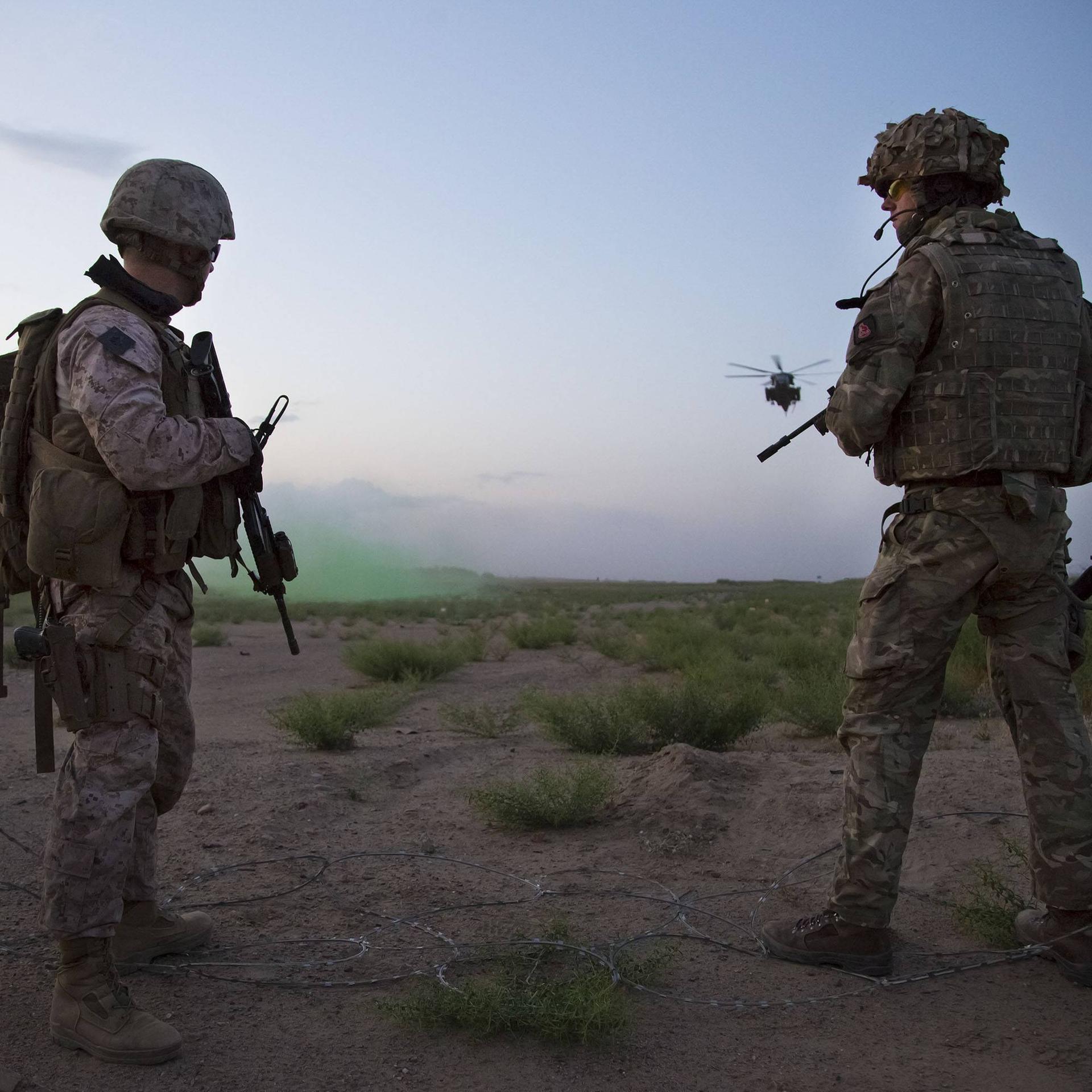 Ein Bild aus dem Jahr 2017 zeigt britische und US-amerikanische Soldaten in Afghanistan. Sie stehen bewaffnet auf einem Feld, im Hintergrund fliegt ein Helikopter.