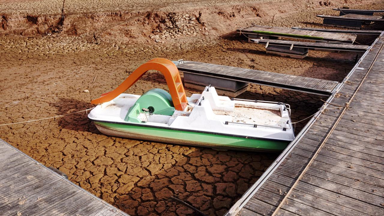 Ein Tretboot mit roter Rutsche liegt an einem Steg auf rissigen Lehm eines ausgetrockneten Sees.