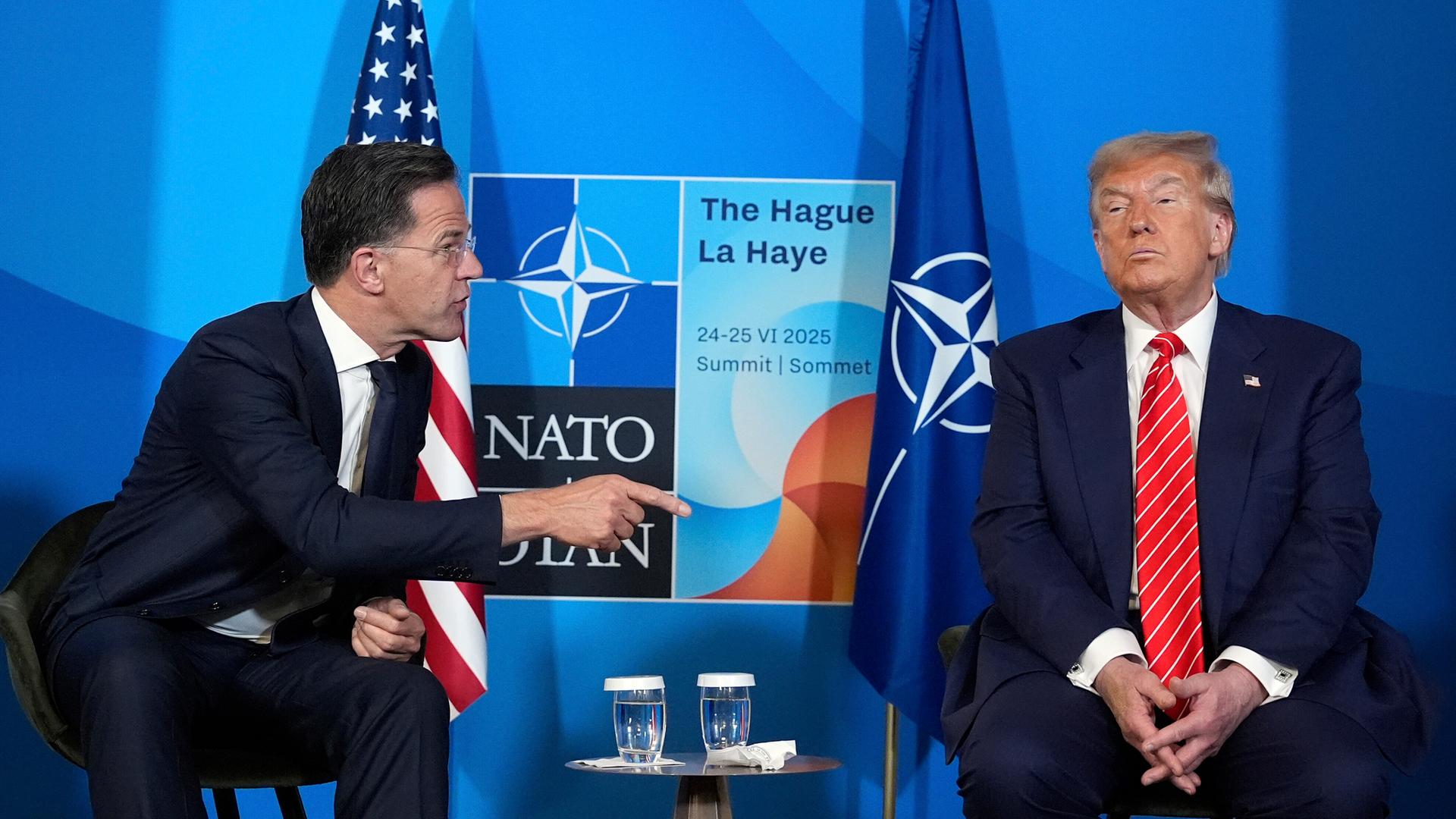 Präsident Donald Trump und NATO-Generalsekretär Mark Rutte unterhalten sich bei einer Pressekonferenz im Rahmen des NATO-Gipfels in Den Haag. Mark Rutte wendet sich Donald Trump mit ausgstrecktem Zeigefinger zu. Im Hintergrund sieht man die NATO-Flagge. Präsident Donald Trump und NATO-Generalsekretär Mark Rutte unterhalten sich bei einer Pressekonferenz im Rahmen des NATO-Gipfels in Den Haag. Mark Rutte wendet sich Donald Trump mit ausgstrecktem Zeigefinger zu. Im Hintergrund sieht man die NATO-Flagge.