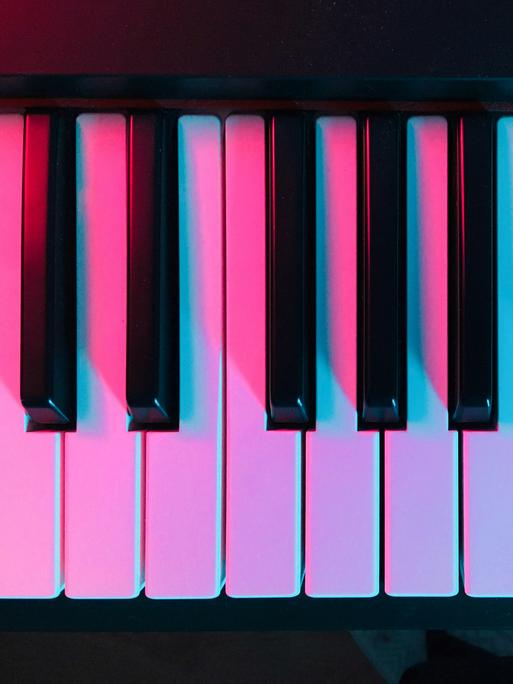 Blick auf moderne Klaviertasten, die in pinkfarbenes Licht getaucht sind.