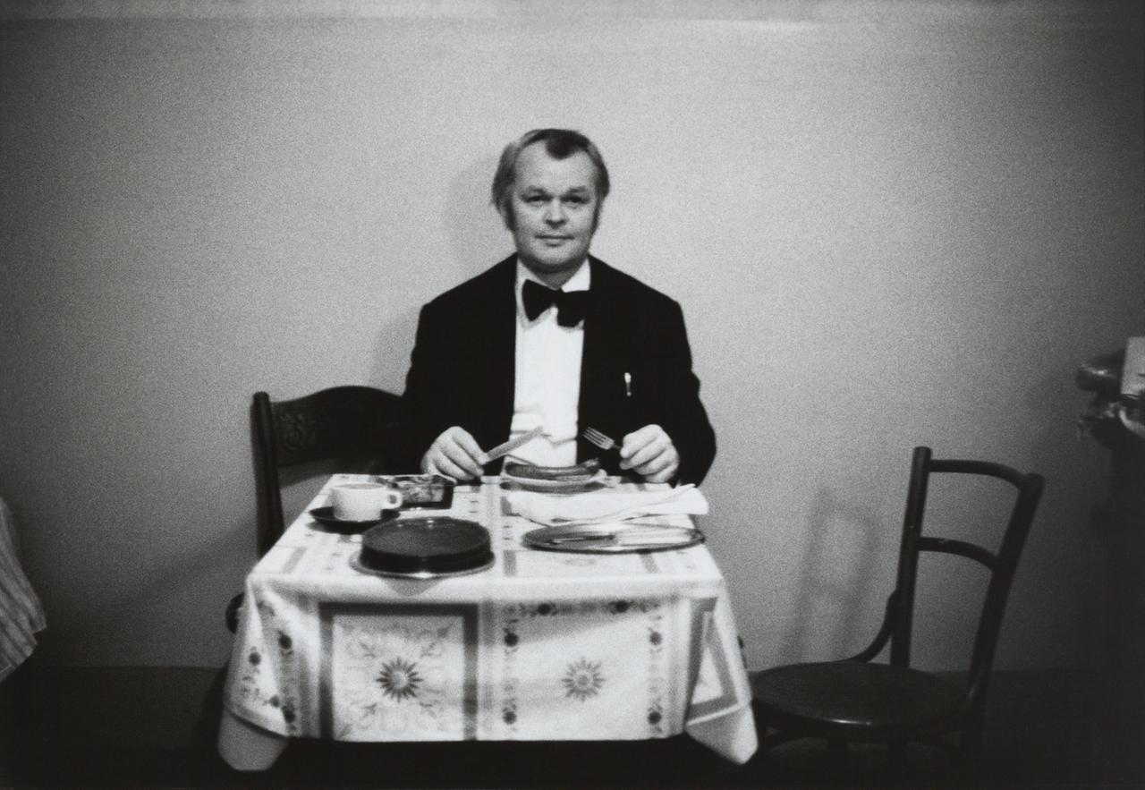 Ein Mann sitzt allein an einem Esstisch mit Besteck in den Händen.