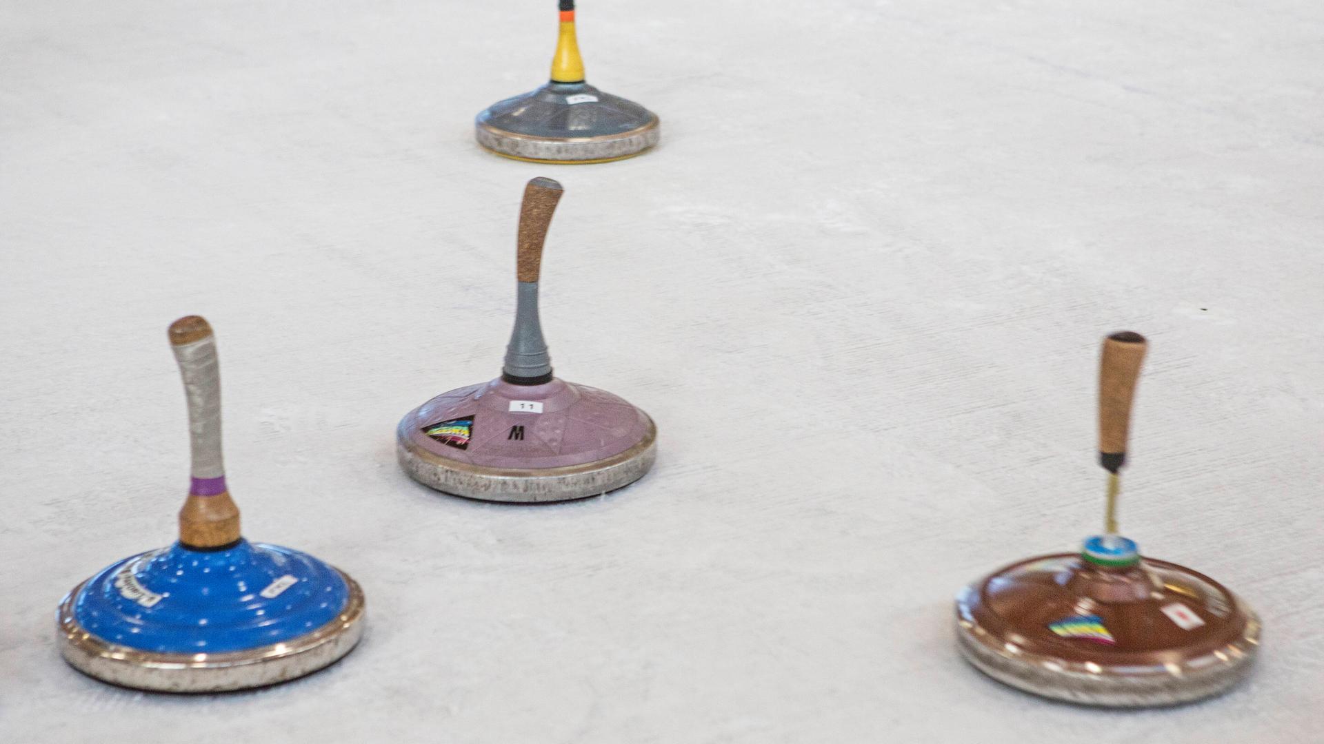 Auf einer Eisfläche sind mehrere Sportgeräte. Es sind Eisstöcke: flache, runde Metallkörper, an denen Holzstöcke befestigt sind.