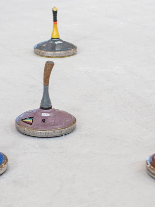 Auf einer Eisfläche sind mehrere Sportgeräte. Es sind Eisstöcke: flache, runde Metallkörper, an denen Holzstöcke befestigt sind.