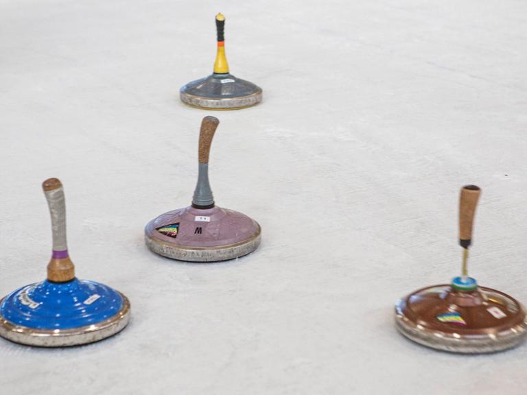 Auf einer Eisfläche sind mehrere Sportgeräte. Es sind Eisstöcke: flache, runde Metallkörper, an denen Holzstöcke befestigt sind.