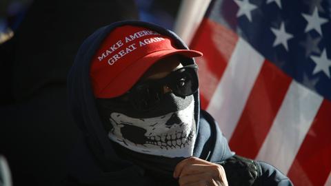 Ein vermummter Mensch mit Sonnenbrille, hochgezogenem Schal und "Make America Great Again"-Basecap protestiert am 10. Januar 2025 vor dem Strafgericht in Manhattan, in dem der designierte US-Präsident Donald Trump verurteilt wurde.