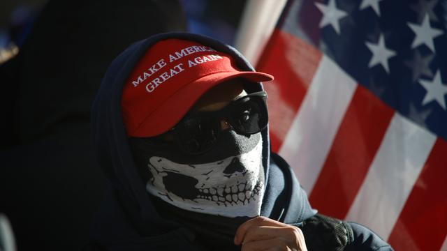 Ein vermummter Mensch mit Sonnenbrille, hochgezogenem Schal und "Make America Great Again"-Basecap protestiert am 10. Januar 2025 vor dem Strafgericht in Manhattan, in dem der designierte US-Präsident Donald Trump verurteilt wurde.