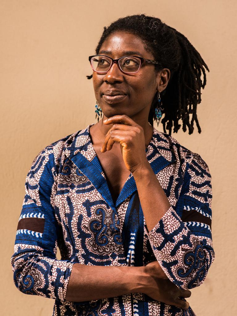 Gloria Boateng stützt das Kinn auf ihre Hand. Sie trägt eine blau gemusterte Bluse und das schwarze Haar in Braids.