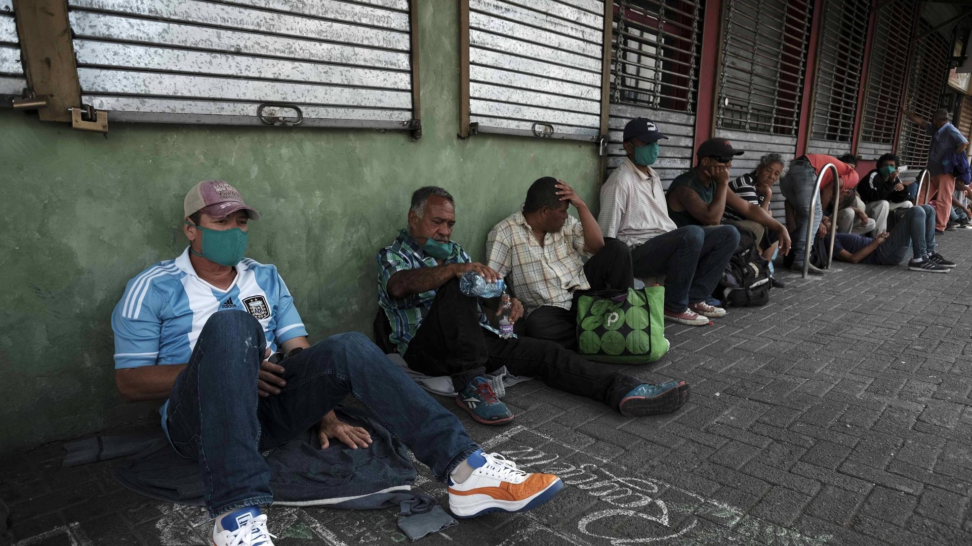 Flüchtlinge sitzen in San Jose in Costa Rica in einer Reihe auf dem Boden.
