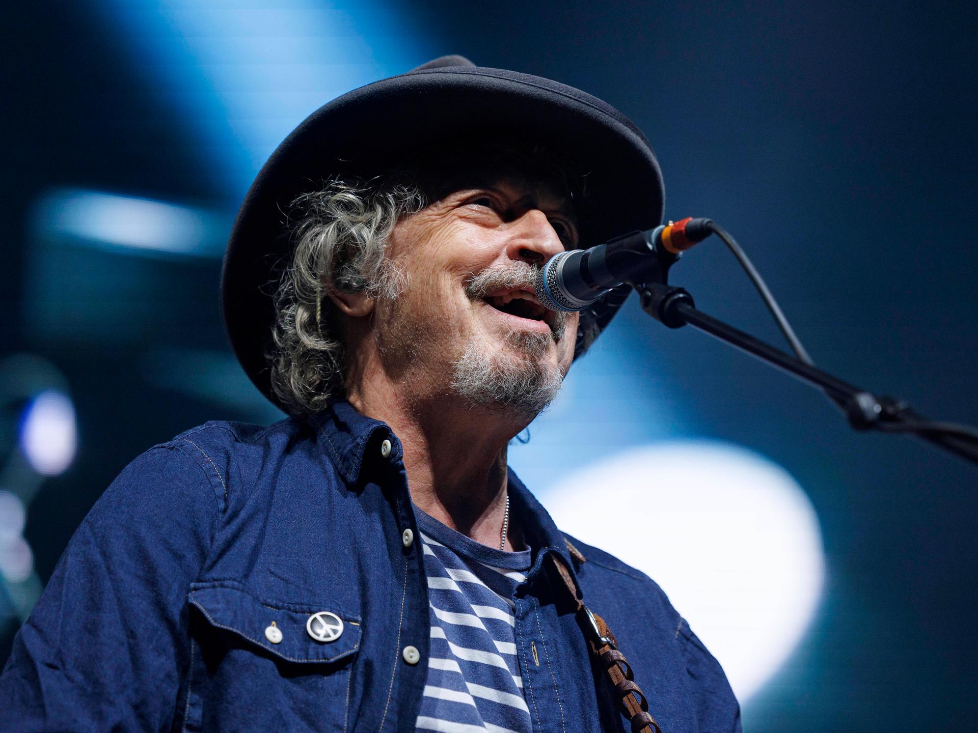 Wolfgang Niedecken singt am 30. März 2022 beim Konzert von Niedeckens BAP in der Lanxess-Arena in Köln in ein Mikrofon. An seinem Jeans-Hemd hängt ein kleiner Button mit Peace-Zeichen.