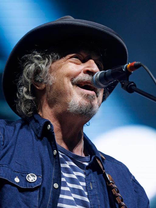 Wolfgang Niedecken singt am 30. März 2022 beim Konzert von Niedeckens BAP in der Lanxess-Arena in Köln in ein Mikrofon. An seinem Jeans-Hemd hängt ein kleiner Button mit Peace-Zeichen.