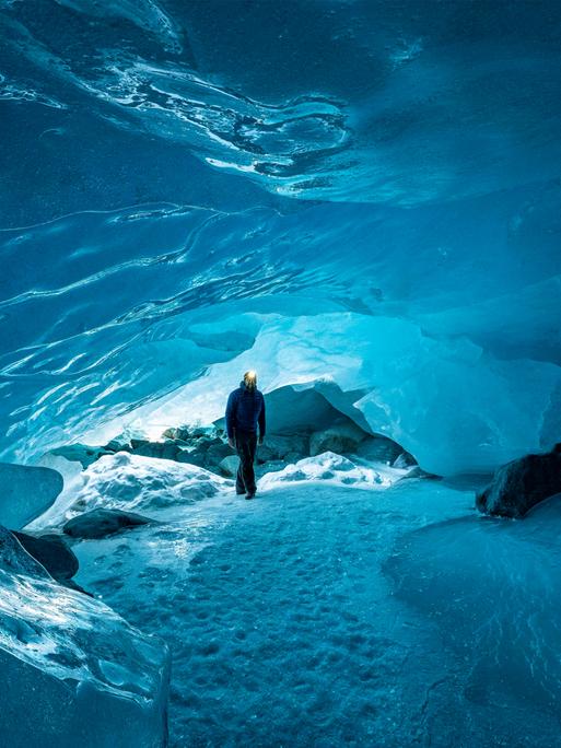 Mann mit Stirnlampe geht in die Gletscherhöhle des Morteratsch-Gletschers in der Schweiz.