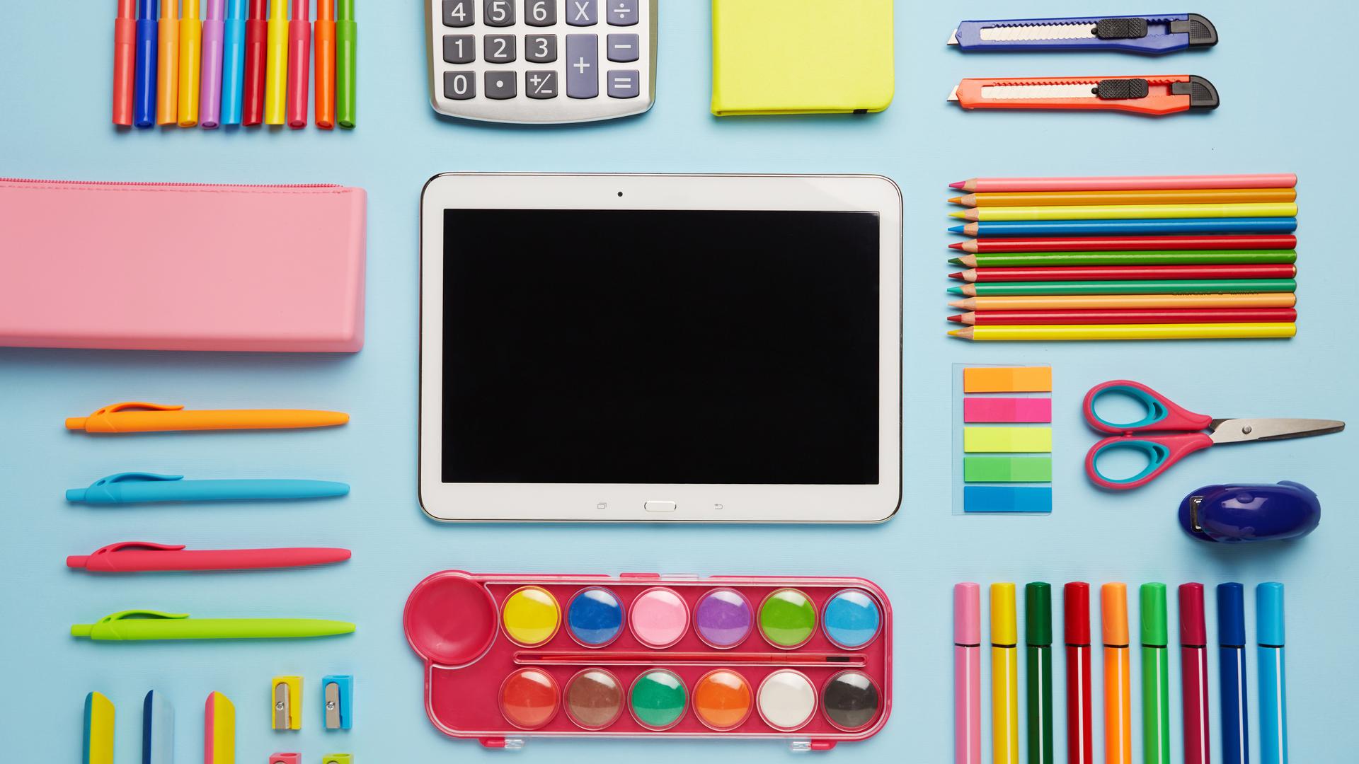 Schulmaterial, Stifte und ein Tablet-Computer liegen auf einem Tisch.