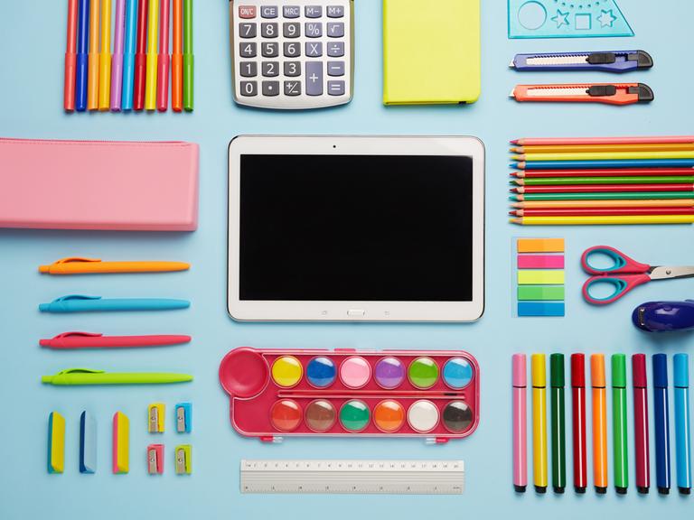 Schulmaterial, Stifte und ein Tablet-Computer liegen auf einem Tisch.