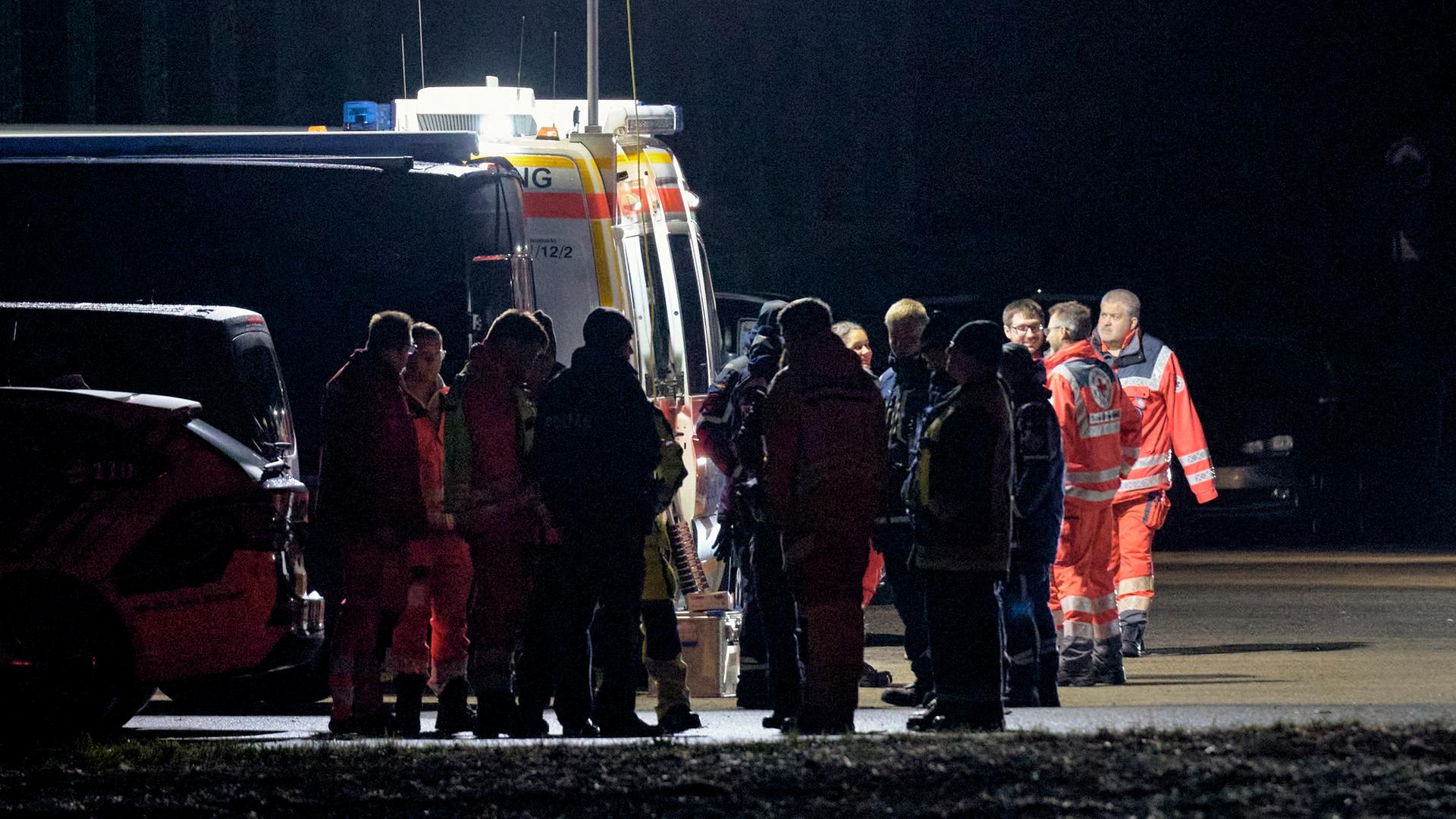 Das Bild zeigt Einsatzkräfte von Polizei und Rettungssanitäterm im Einsatz bei Nacht. Die Szenerie ist von einem hellen Scheinwerfer erleuchtet.. 