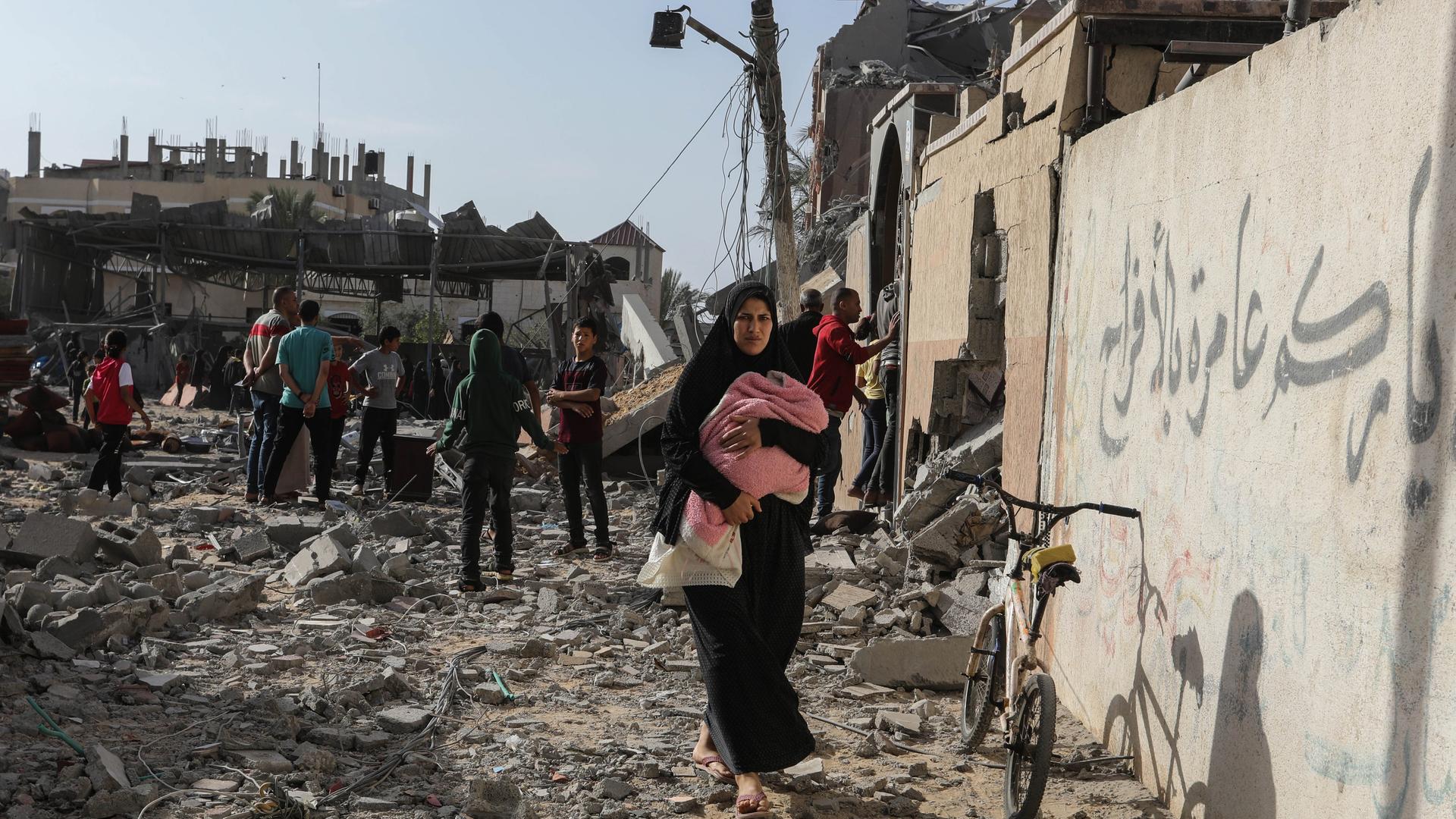 Palästinenser inspizieren beschädigte Häuser, nachdem israelische Kampfflugzeuge ein Haus bombardiert hatten. Im Vordergrund ist eine Frau mit einem Kind auf dem Arm.