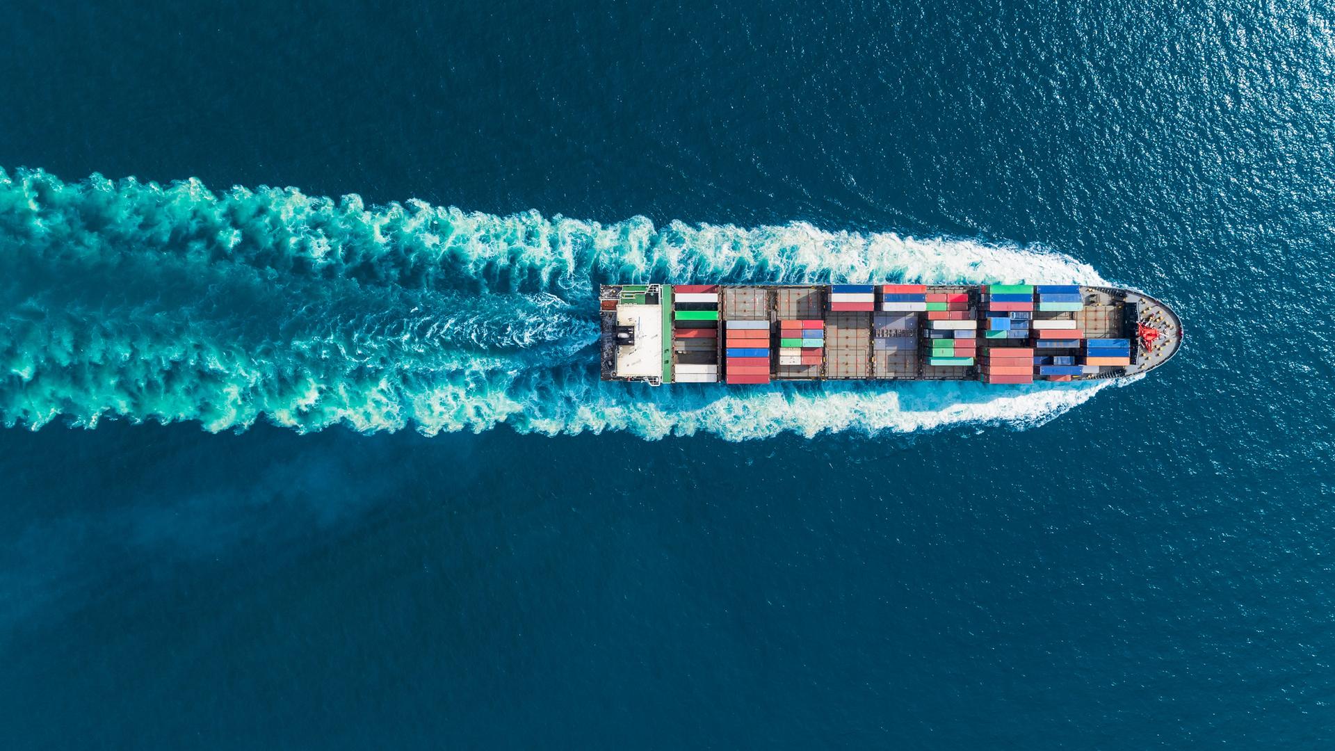 Aerialaufsicht von einem Containerschiff im Meer in voller Geschwindigkeit.