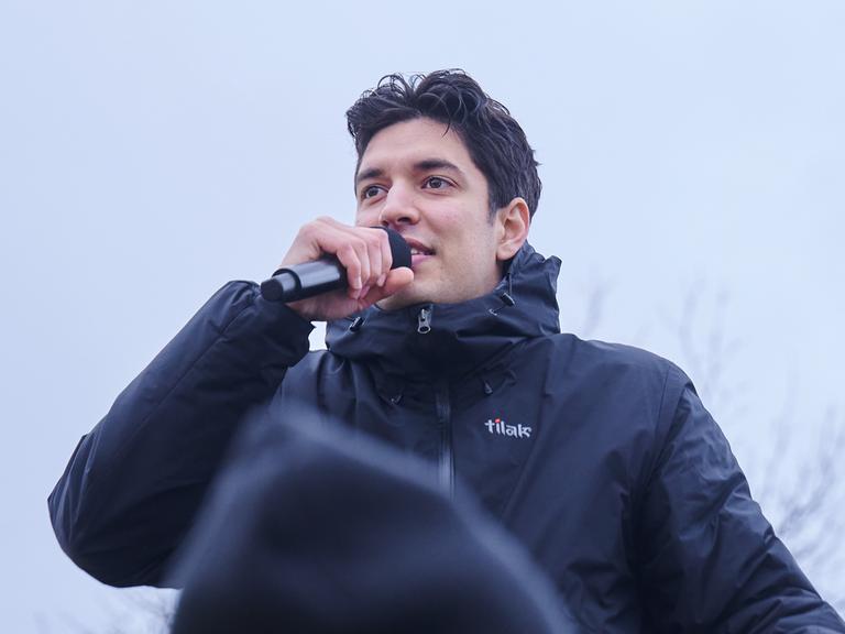 Apsilon, Influencer und Sänger singt während einer Demonstration gegen rechts auf einer Bühne. Er trägt eine schwarze Jacke und hält ein Handmikrofon vor den Mund. 