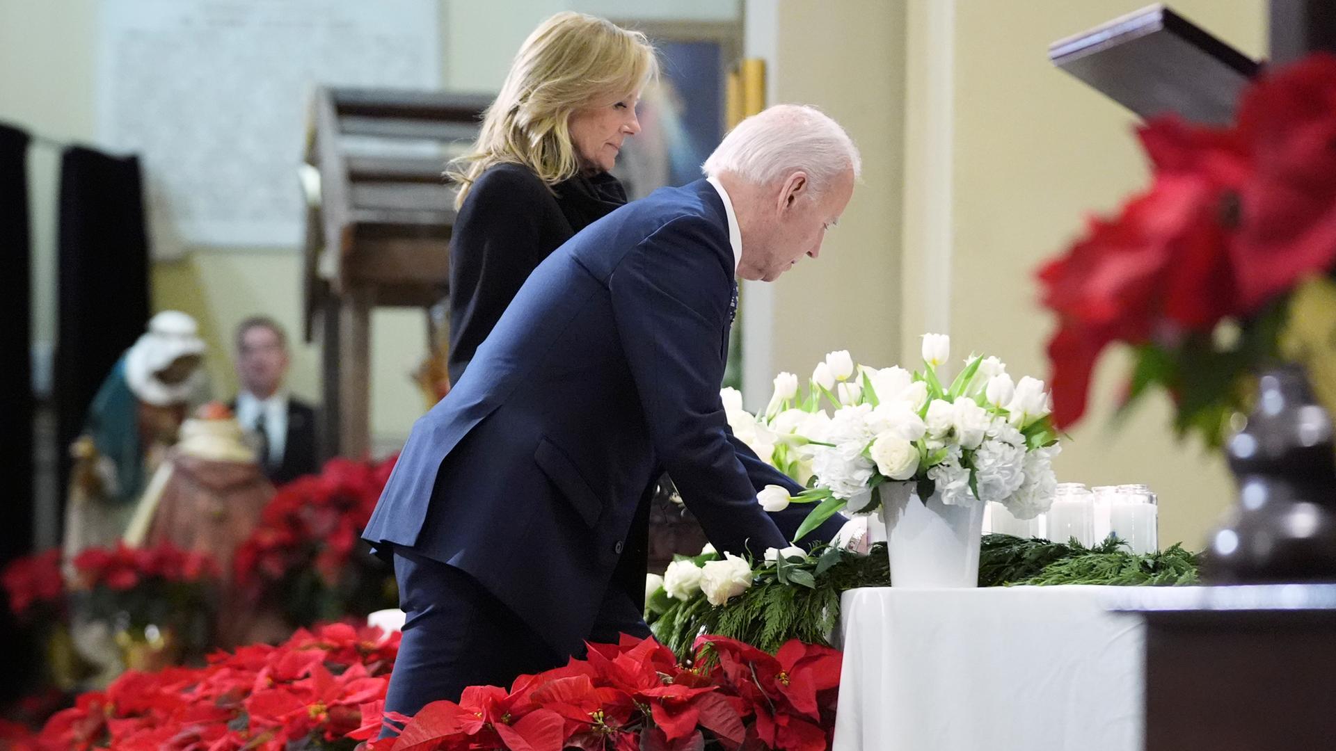 Die beiden stellen inmitten roter und weißer Blumen die Kerze auf einen Altar mit Kreuz.