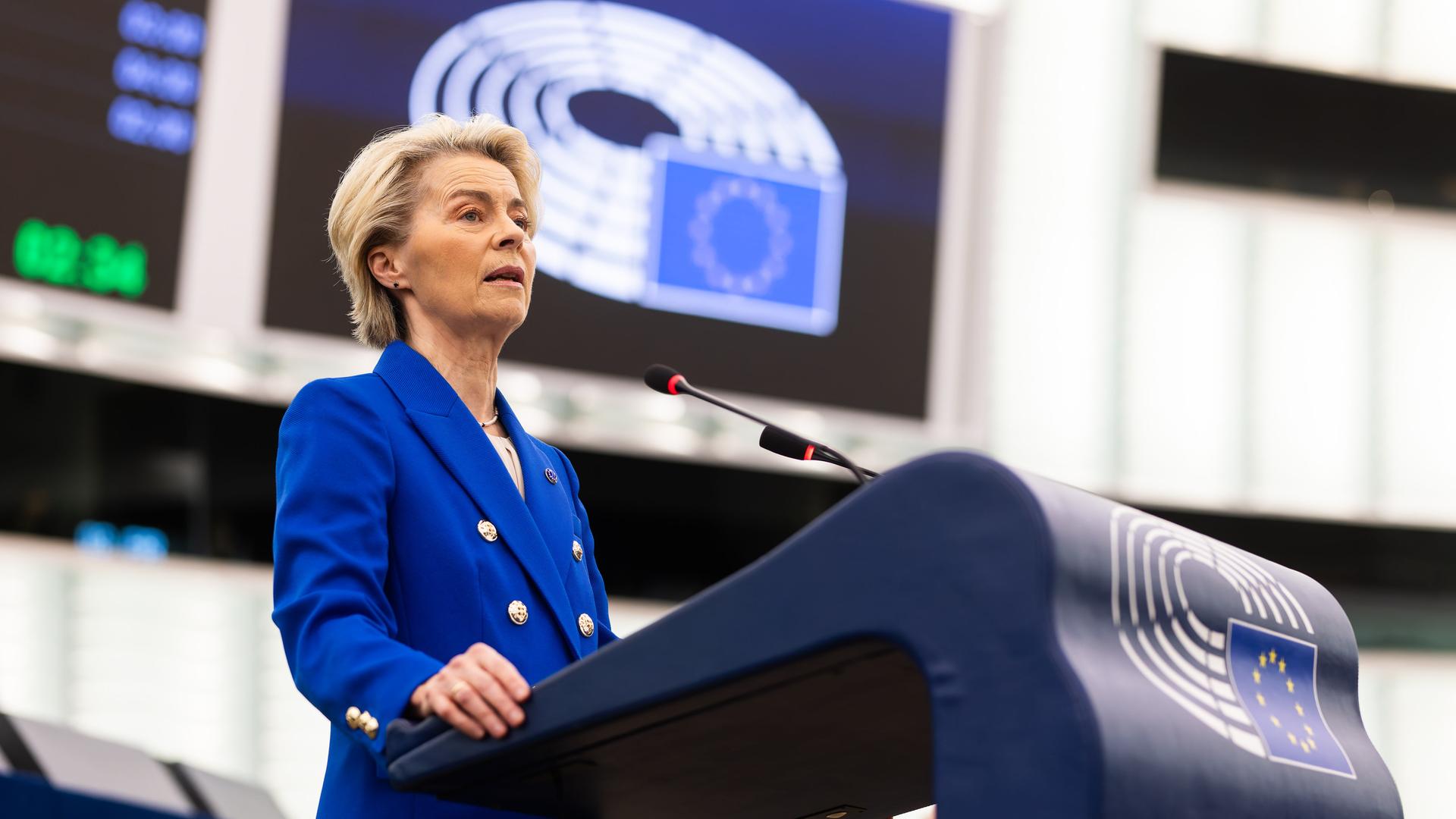 Von der Leyen im blauen Jackett steht im Plenarsaal des Europäischen Parlaments und spricht. 