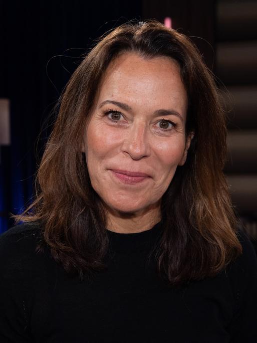 Portraitfoto der Moderatorin Anne Will, gekleidet in Schwarz vor dunklem Hintergrund