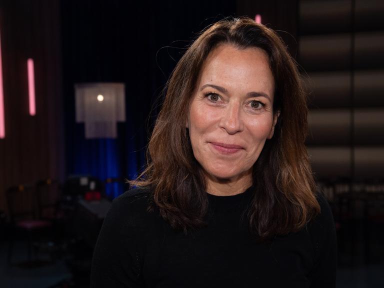 Portraitfoto der Moderatorin Anne Will, gekleidet in Schwarz vor dunklem Hintergrund