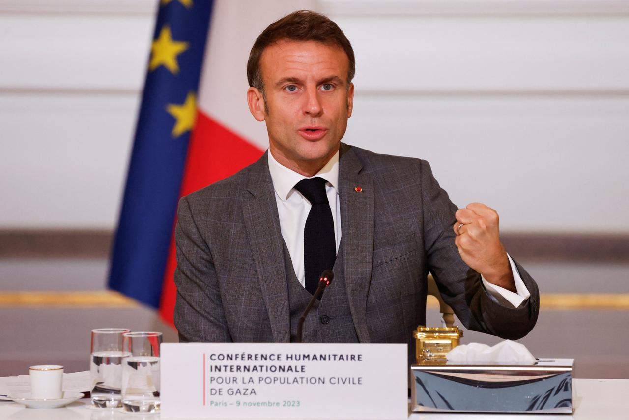 Der französische Präsident Macron spricht bei der Nahost-Konferenz in Paris. Er sitzt an einem Tisch und ballt die linke Hand zur Faust. Hinter ihm die EU-Fahne.