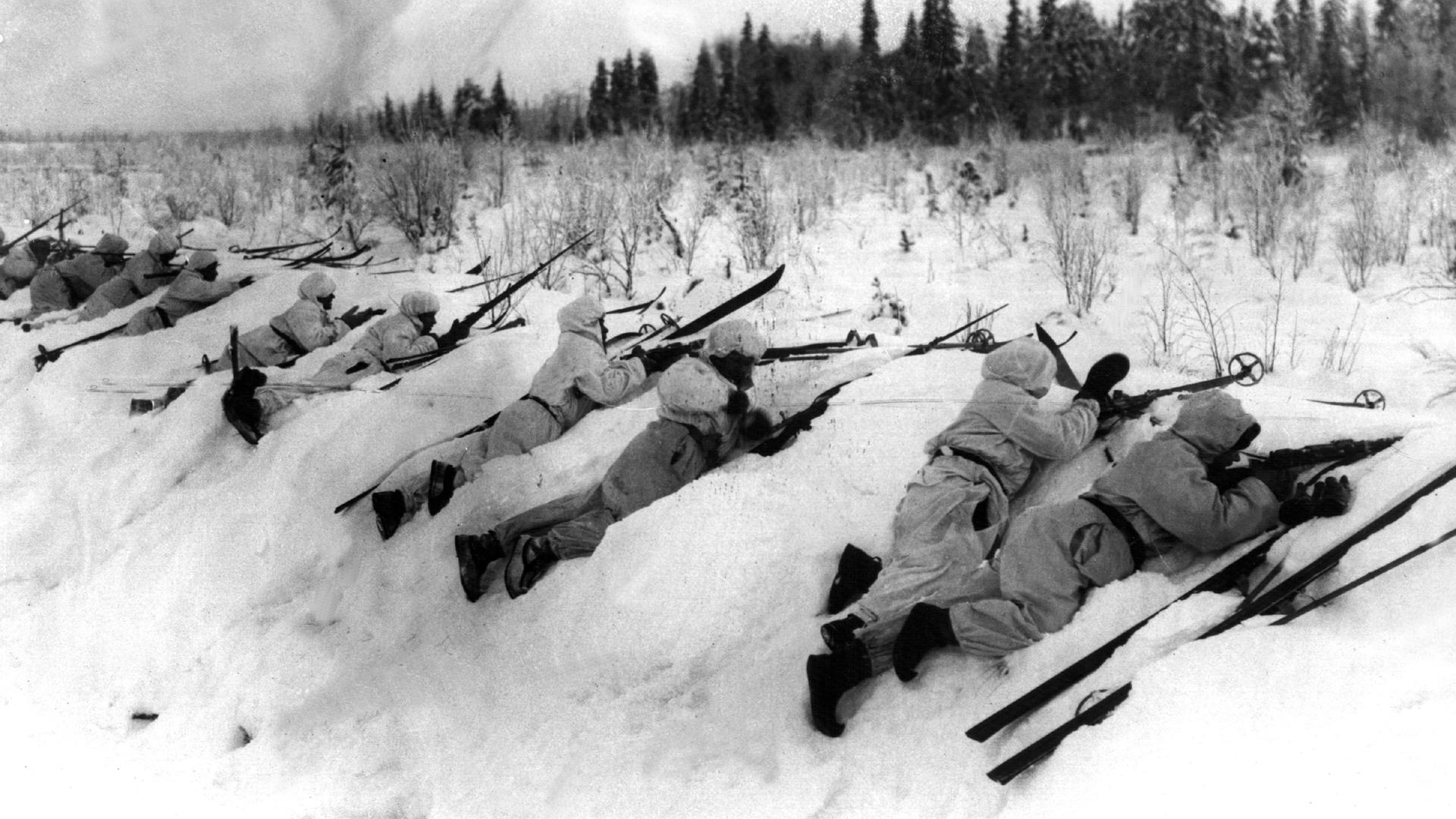 Eine historische Schwarz-Weiß-Aufnahme aus dem Winterkrieg 1939 zeigt, wie sich finnische Truppen in Schneeuniformen an der Frontlinie gegen russische Angriffe verteidigen. 