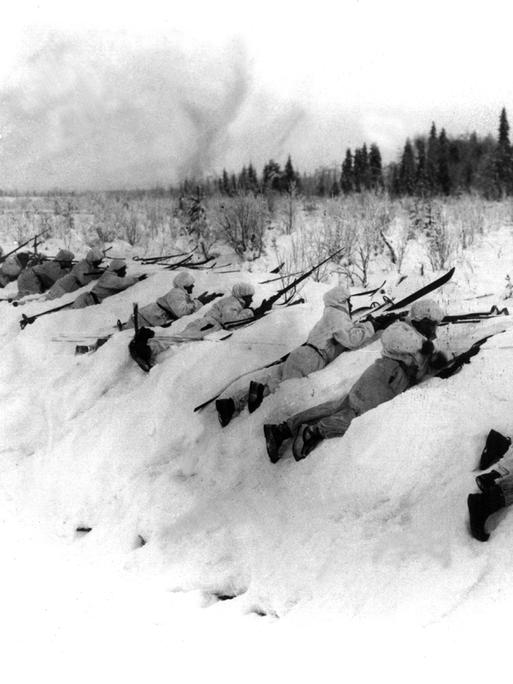 Eine historische Schwarz-Weiß-Aufnahme aus dem Winterkrieg 1939 zeigt, wie sich finnische Truppen in Schneeuniformen an der Frontlinie gegen russische Angriffe verteidigen. 