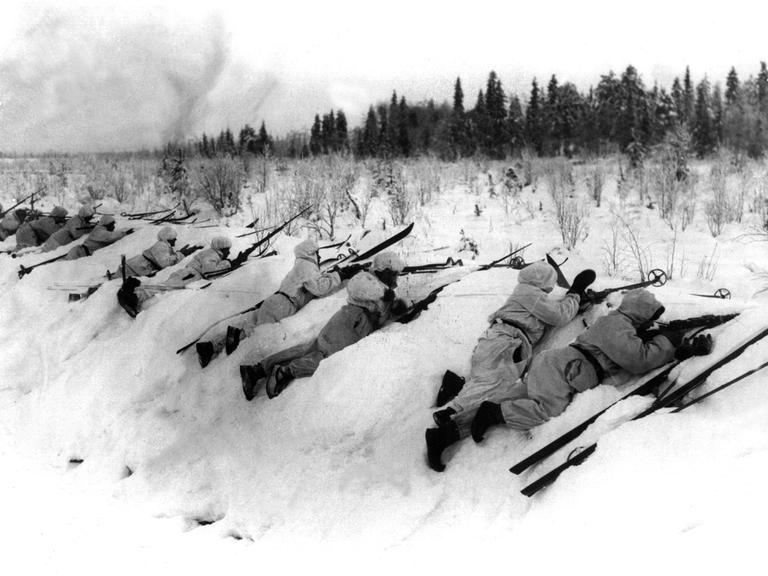 Eine historische Schwarz-Weiß-Aufnahme aus dem Winterkrieg 1939 zeigt, wie sich finnische Truppen in Schneeuniformen an der Frontlinie gegen russische Angriffe verteidigen. 