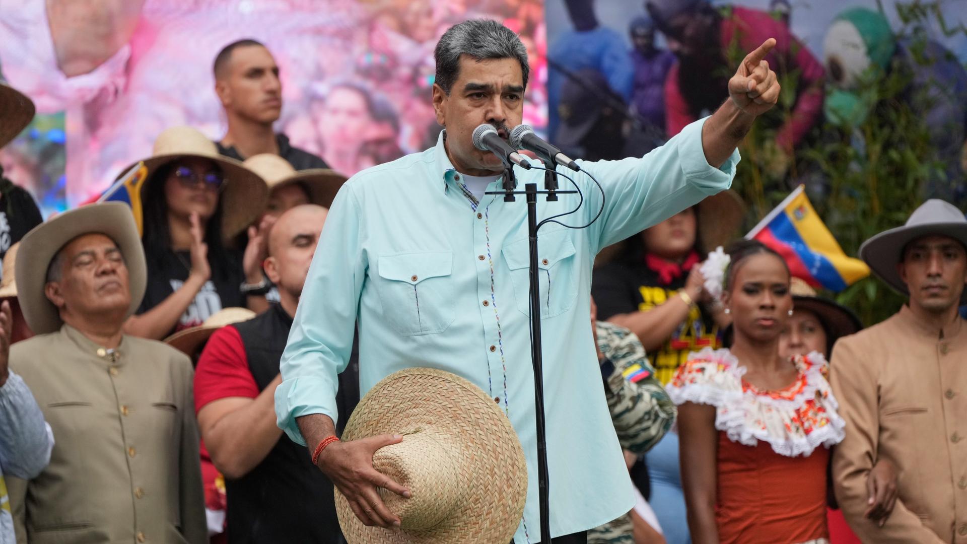 Nicolas Maduro spricht in ein Mikrofon, hebt die eine Hand und trägt in der anderen einen Strohhut Nicolas Maduro spricht in ein Mikrofon, hebt die eine Hand und trägt in der anderen einen Strohhut