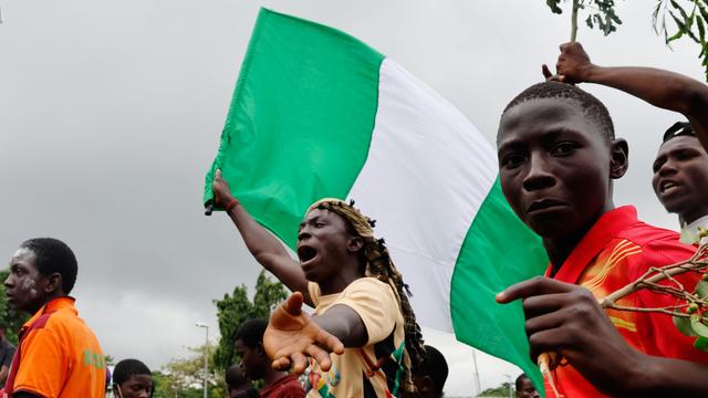 Ein Jugendlicher hält die grün-weiße nigerianische Flagge in der Hand und schreit. Rechts neben ihm blickt ein weiterer Jugendlicher in die Kamera.