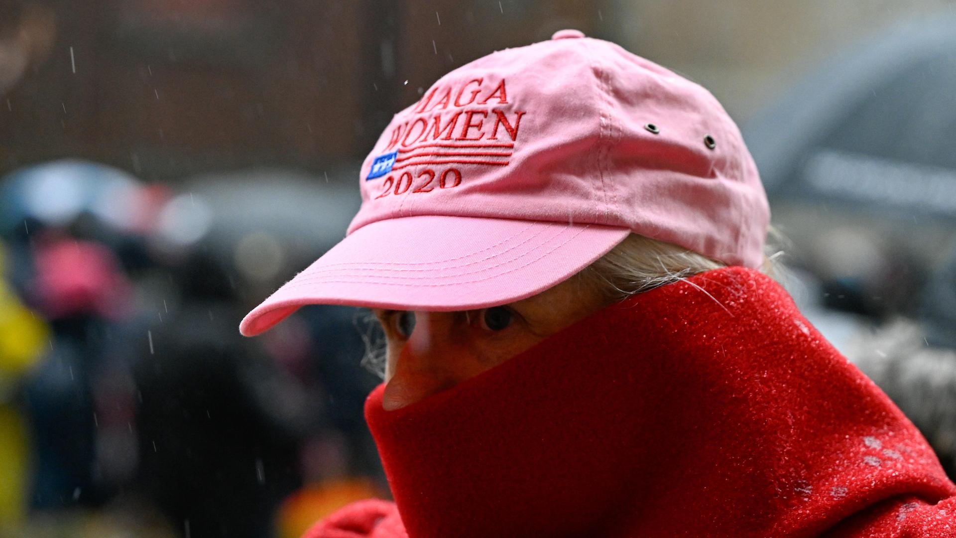 Eine Frau trägt eine pinkte Baseballmütze mit der Aufschrift "Maga Women" und einen Schal vor dem Gesicht, um sich vor der Kälte zu schützen.