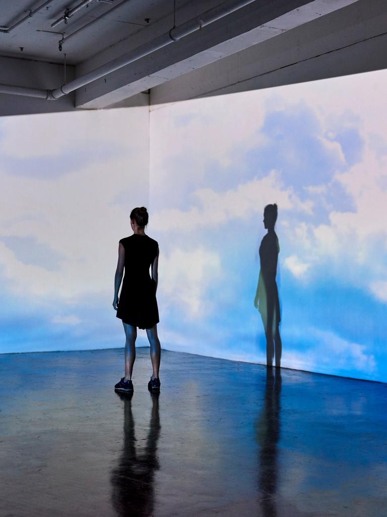 Eine junge Frau in einem Museum schaut auf eine Wand, an die große Bilder vom bewölkten Himmel projiziert werden.