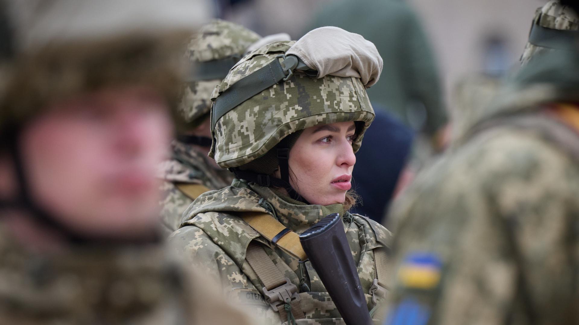 Eine uniformierte und bewaffnete Soldatin steht zwischen ihren Kameraden in der ukrainischen Armee.