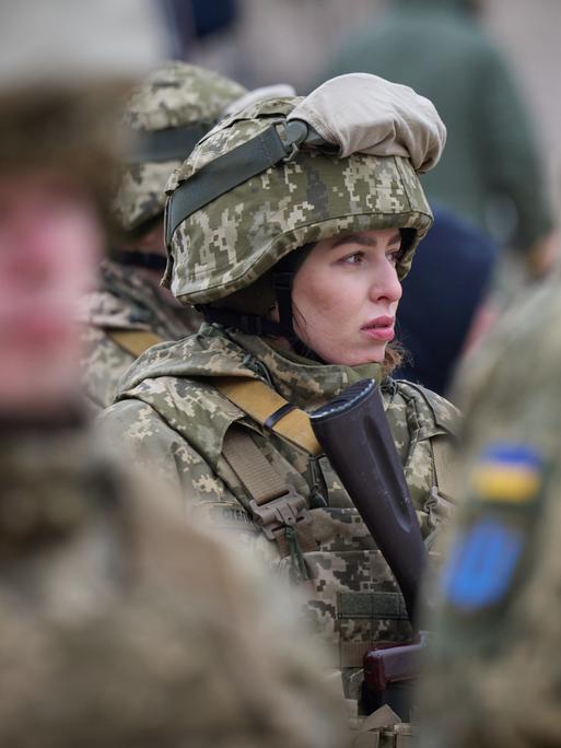 Eine uniformierte und bewaffnete Soldatin steht zwischen ihren Kameraden in der ukrainischen Armee.