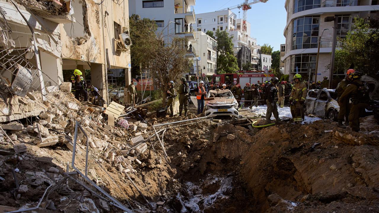 Israelische Sicherheitskräfte stehen vor einem großen Loch in der Straße. Die benachbarten Häuser sind beschädigt. 