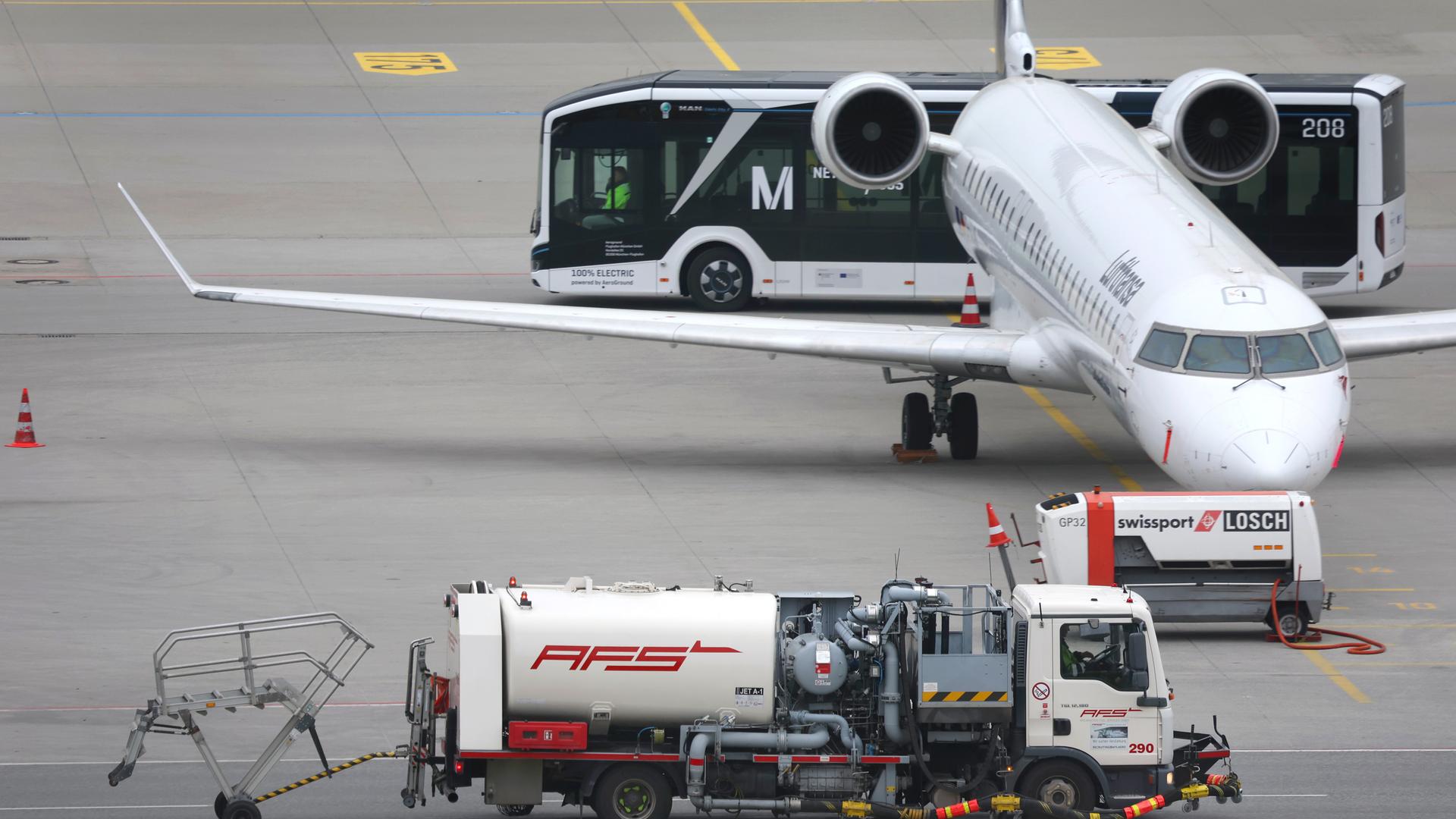 Ein Tankfahrzeug (vorne) fährt auf dem Vorfeld des Flughafens München an einem Passagierflugzeug vorbei. Ein Tankfahrzeug (vorne) fährt auf dem Vorfeld des Flughafens München an einem Passagierflugzeug vorbei.