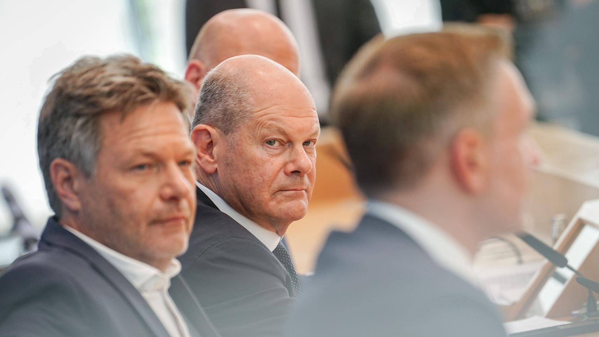 Bundeskanzler Olaf Scholz, Wirtschaftsminister Robert Habeck und Finanzminister Christian Lindner sitzen bei einer Pressekonferenz hintereinander. Scholz schaut grimmig in Richtung seiner Minister.