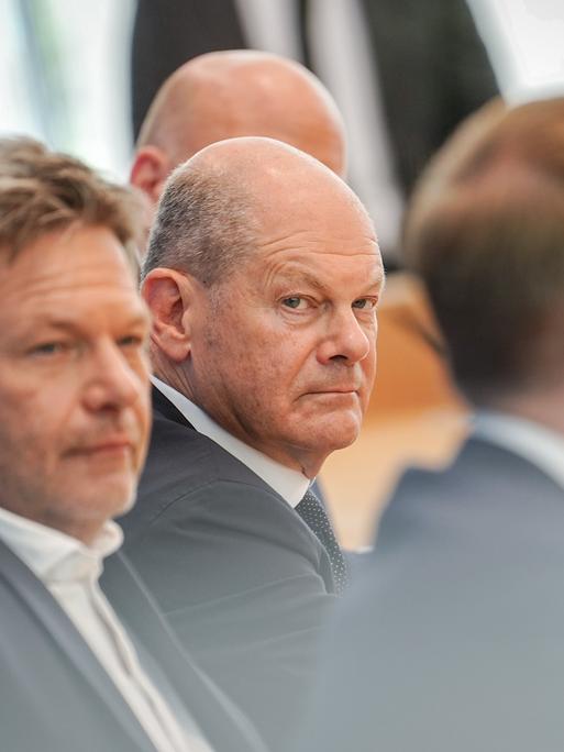 Bundeskanzler Olaf Scholz, Wirtschaftsminister Robert Habeck und Finanzminister Christian Lindner sitzen bei einer Pressekonferenz hintereinander. Scholz schaut grimmig in Richtung seiner Minister.