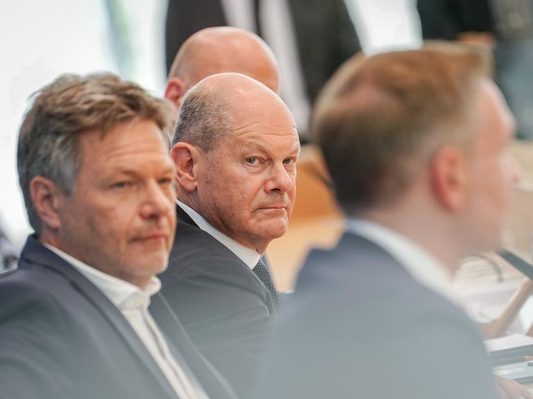 Bundeskanzler Olaf Scholz, Wirtschaftsminister Robert Habeck und Finanzminister Christian Lindner sitzen bei einer Pressekonferenz hintereinander. Scholz schaut grimmig in Richtung seiner Minister.