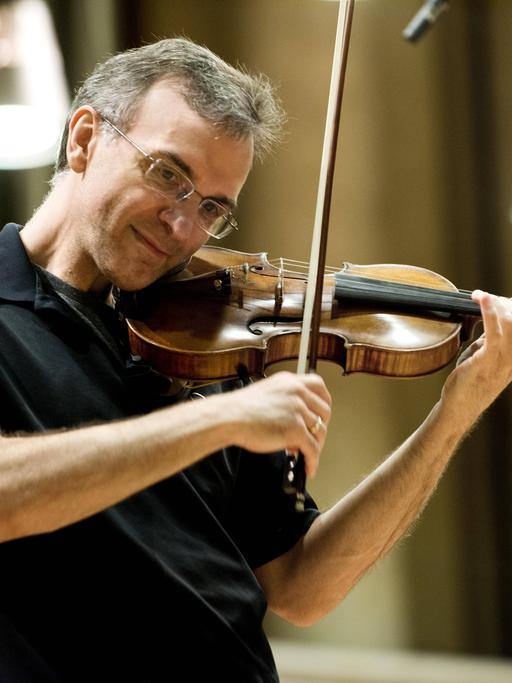 Der Geiger Gil Shaham trägt ein schwarzes Polohemd und spielt etwas auf seiner Geige.