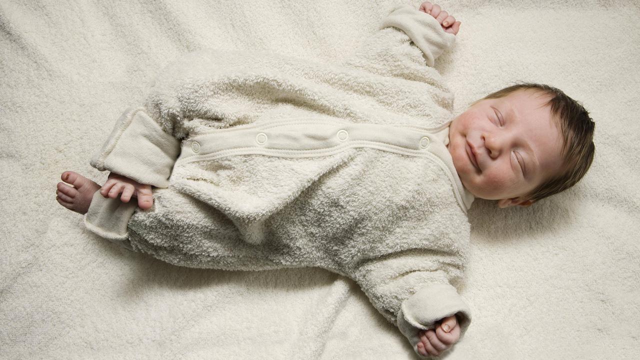 Ein schlafendes Neugeborenes im Kuschelanzug mit ausgestreckten Armen.