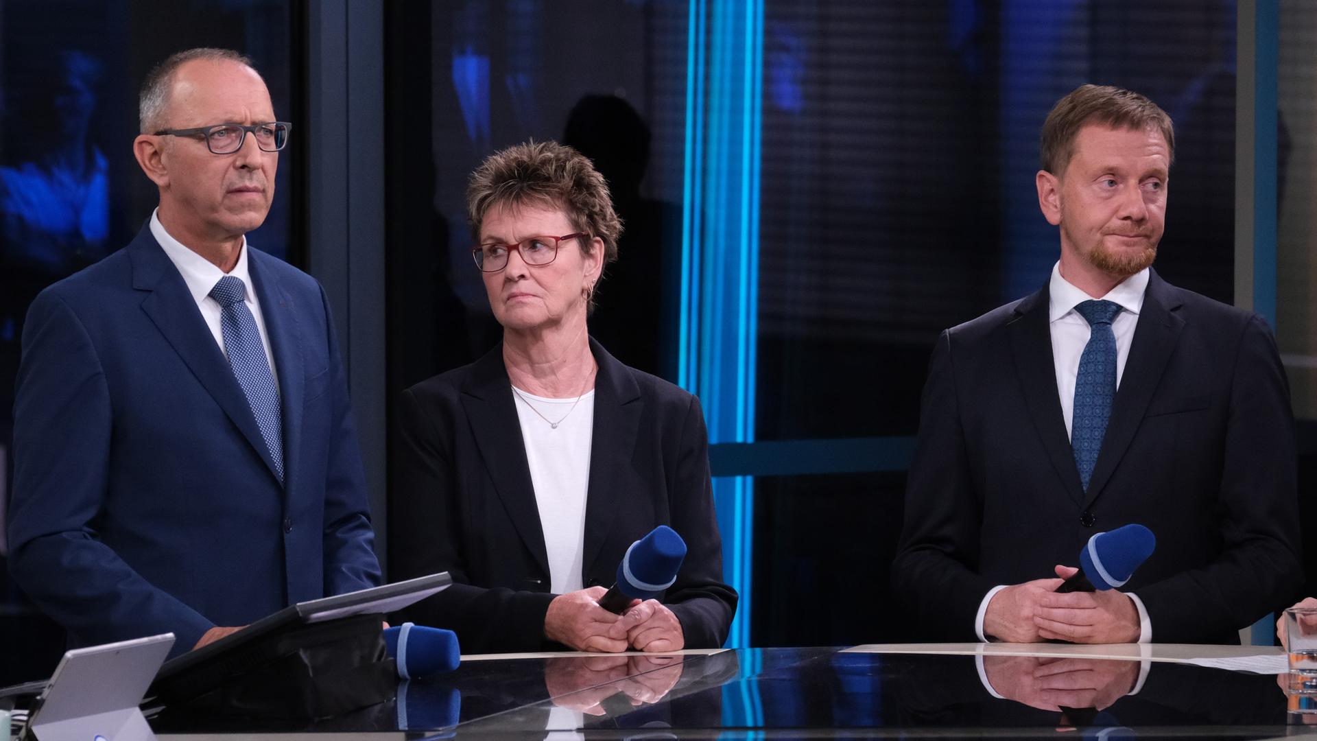 AfD-Spitzenkandidat Jörg Urban, BSW-Spitzenkandidatin Sabine Zimmermann und Michael Kretschmer (CDU), amtierender Ministerpräsident von Sachsen stehen mit ernstem Blick nebeneinander in einem Fernsehstudio.