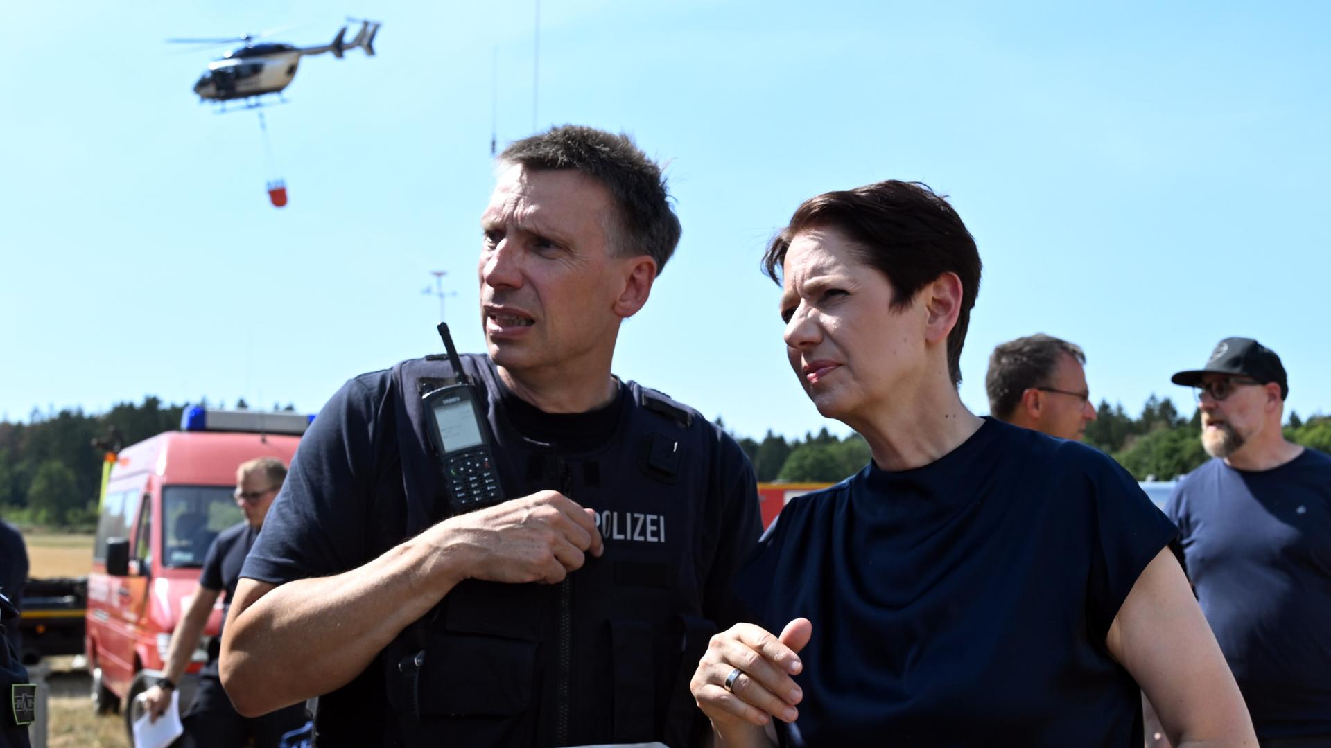 Silke Gorißen (rechts im Bild), Ministerin für Landwirtschaft und Verbraucherschutz des Landes Nordrhein-Westfalen, steht mit einem Polizeibeamten vor der Einsatzzentrale beim Waldbrand im Hürtgenwald. Im Hintergrund fliegt ein Löschhubschrauber vorbei. Silke Gorißen (rechts im Bild), Ministerin für Landwirtschaft und Verbraucherschutz des Landes Nordrhein-Westfalen, steht mit einem Polizeibeamten vor der Einsatzzentrale beim Waldbrand im Hürtgenwald. Im Hintergrund fliegt ein Löschhubschrauber vorbei.