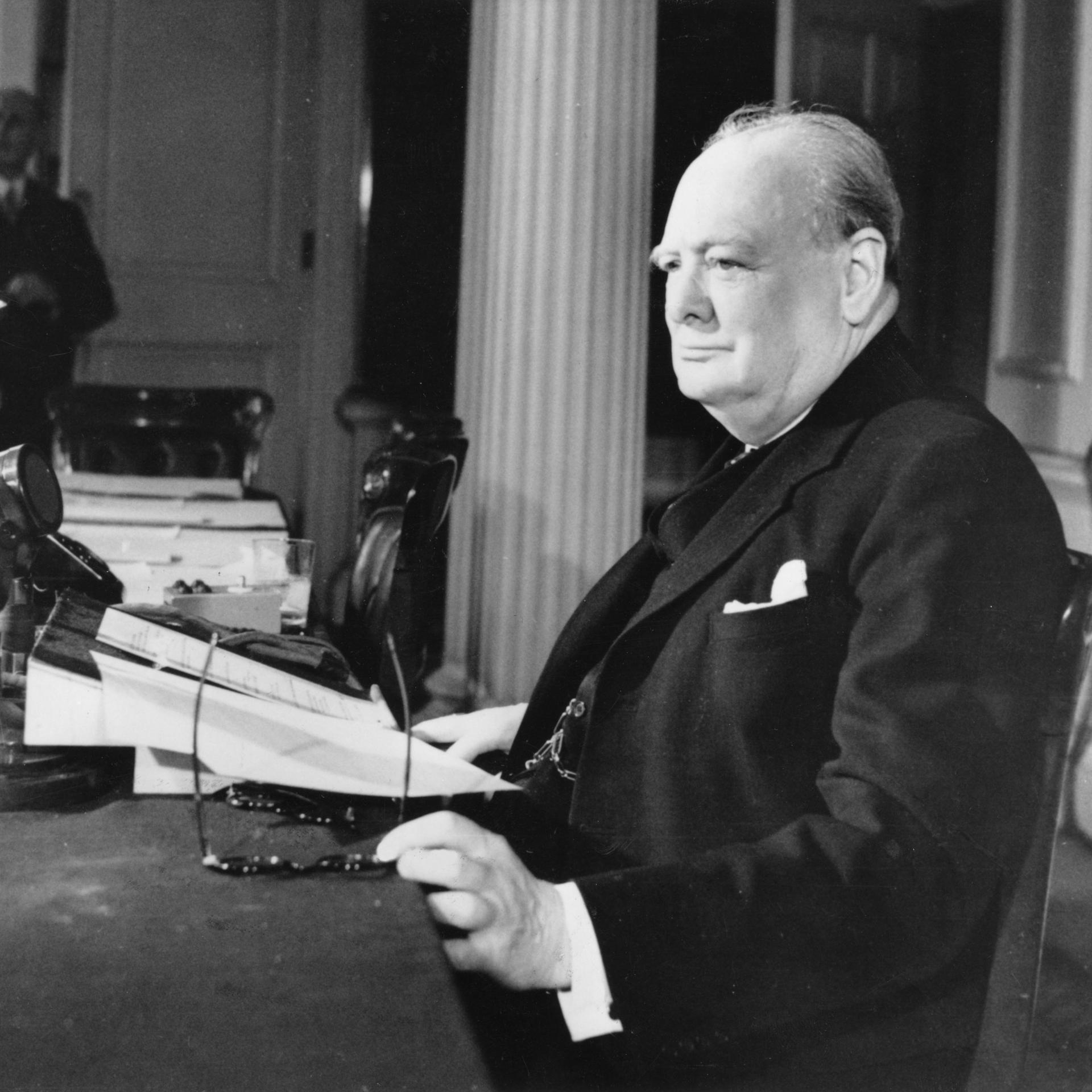 Winston Churchill sitzt mit einer Zeitung an einem Schreibtisch