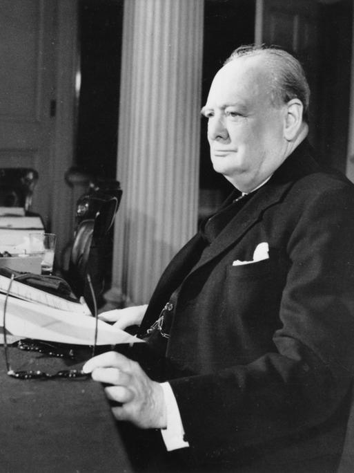 Winston Churchill sitzt mit einer Zeitung an einem Schreibtisch