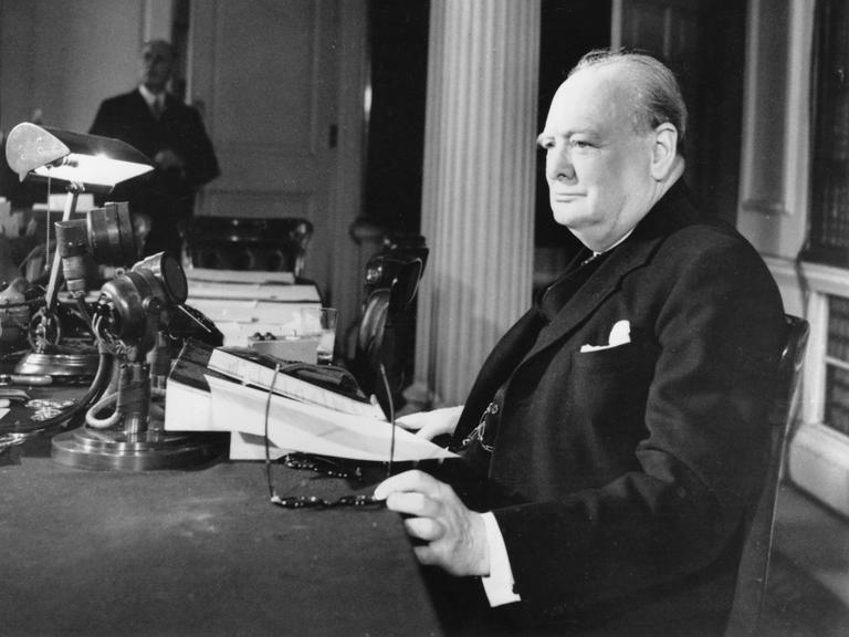 Winston Churchill sitzt mit einer Zeitung an einem Schreibtisch