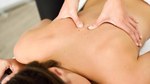 Zwei Hände massieren den Rücken einer Frau, die auf dem Bauch einer Massageliege liegt. Zwei Hände massieren den Rücken einer Frau, die auf dem Bauch einer Massageliege liegt.
